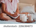 Small photo of Notebook, writing and woman with home candles for healing journal, calm planning or self care inspiration in bedroom. Creative person or writer for mindfulness goals, meditation or peace notes in bed