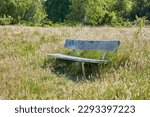 An old wooden bench in an open field outside with a forest in the background. Find a quiet place to enjoy the beauty of nature. The woods can be a peaceful and tranquil place when you need to be alone