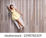 Young woman, sunbed and luxury summer resort, vacation or holiday to relax outdoors and lounge in the spring sun. Girl, sleeping on tanning bed and top view of modern wood deck in background