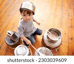 Small photo of Portrait, boy child playing drums on pots on a floor, curious and enjoying music. Face, top view and kid with pans for musical entertainment, silly and carefree in kitchen in his home on the weekend