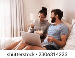 Small photo of Laptop, watching movie and popcorn with laughing couple in bed for streaming, relax or internet. Subscription, happy or comic man and woman at home for social media, funny and free time on weekend