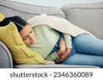 Small photo of Stomach pain, pms and woman on a sofa with stress, bad or gut health, gas or ibs in her home. Abdomen, anxiety and female person in living room with gas, digestion or constipation from endometriosis