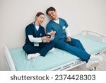Small photo of Doctors, smartphone and break on hospital bed, relax and happy from healthcare service, job and career. Nurse, man and woman for rest, shift and employee for social media, memes and communication