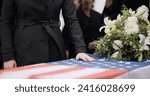 Small photo of USA veteran funeral, woman and casket with touch, sad family and flag for mourning, depression and respect. Widow, people and army service with coffin, burial or memorial for war hero in Philadelphia