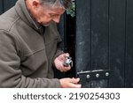 Small photo of Rural crime. A farmer inspects the damage after a break in. Holding a twisted padlock. A black padlock with a bent shackle destroyed during a barn break in. Agricultural farm theft of machinery.