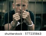 Small photo of Handcuffed teenage boy behind bars in a prison cell staring intently at the camera unrepentant of his criminal behavior