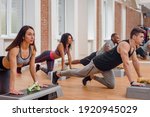 Small photo of Group of athletic sporty men and women doing stretching exercise with steppers