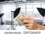Small photo of Professional male photographer getting payment for photo session, The composition juxtaposes the tangible representation of income with the creative space