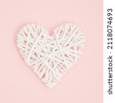 Small photo of A heart made of knitted white wicker on a pastel pink background. Minimal creative concept of decorative infatuation, love, Valentine's Day, weddings.
