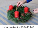Woman lighting festive red advent candles on a traditional homemade evergreen pine Christmas wreath with cones, close up view