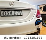 Small photo of Sydney, Australia - Jun 14, 2018: Close-up view of a white Mercedes Benz in the process of being electrically charged (lower right plug), in the showroom of Tynan Motors, Miranda.