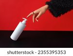 Womans hand in fur coat on a red-black background touches a bottle of cream. Sale concept
