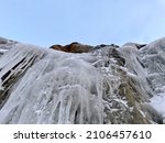 Small photo of Ice and icicles on a stone selvage. Frozen river's small waterfall in a daylight
