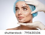 Beauty portrait of woman in blue cap looking aside, plastic surgery concept, studio. Hands in white gloves holding face of model with puncture lines, indoors