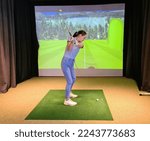Small photo of Girl playing golf on screen and golf simulator. Young golfer playing golf video game indoors