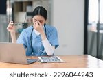 Small photo of Professional millennial female doctor or nurse working on laptop computer and clipboard with a tense expression while sitting at a desk