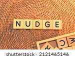 Small photo of NUDGE word text from wooden cube block letters on braided rattan mats background. Nudge meaning is to push against gently, especially in order to gain attention or give a signal.
