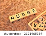 Small photo of NUDGE word text from wooden cube block letters on braided rattan mats background. Nudge is a verb meaning to push slightly or gently, specifically with an elbow when doing so literally.