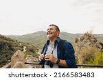 Small photo of Happy senior man looking at the view while standing on a hilltop with binoculars. Cheerful elderly man enjoying a leisurely hike outdoors. Mature man enjoying recreational activities after retirement.