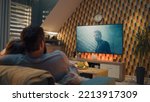 Small photo of Couple on sofa in living room, watching action movie on TV or criminal blockbuster on streaming service, talking and discussing acting, resting at home on weekend. Home theater in modern apartment.