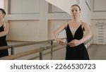 Small photo of Graceful adult ballerina in training bodysuit rehearses near ballet barre and practices classical ballet movements in dance studio. Female ballet dancer on choreography rehearsal. Ballet dance school.