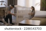 Small photo of Loving parents together assembling white crib for newborn baby at nursery. Young father uses hex key for fixing mounts. Caring wife helps beloved man. Concept of parenthood, childhood and family.
