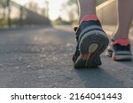 Small photo of Runner's shoes advancing in the tread. Close-up image of some orange sneakers and black and white soles that tread on the asphalt of a bridge over the river with the sunset ahead.