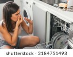 Woman making gestures of bad smell when opening her automatic dishwasher. Young girl with a face of disgust and holding her nose at the malfunction of one of her appliances.