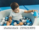 Small photo of Toddler boy playing with a toy while sitting in a ball pit full of colorful balls. A ball pit - a great place for kids to jump, crash, and wiggle. Sensory play at the nursery school. High quality