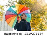 Grey-haired middle-aged man in formal clothes walking around city park holding rainbow umbrella looking up. Horizontal outdoor shot. High quality photo
