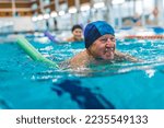 Small photo of Portrait of smiling happy positive white senior adult man with blue swimming swim cap on his head using foam green pool noodle. Indoor shot. Sports area. High quality photo