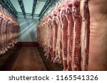 Small photo of Pig carcass cut in half hanging off the hooks in slaughterhouse. Chopped pigs in meat factory. Stored cold raw meat.