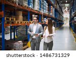 Two successful business people walking through large warehouse center. Manager smiling and looking shelves full with packages and products. Warehouse workers talking about logistics and distribution.