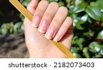 Small photo of Woman's hand natural long nails holding nail file, showing natural nail growth