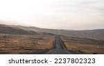 Vintage photo of a country road. Empty road through the desolate hilly area. Cloudy sky and horizon in a haze. Concept landscape. Rural scene.