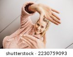 Young blonde laughing girl stands in front of metal wall and makes frame with hands, focused