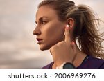 Serious young sporty female touching TWS earbuds while listening to music during outdoor fitness training