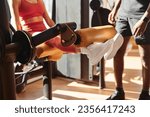 Crop anonymous female athlete doing leg extension on machine during workout with black coach in gym on sunny day