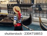 A woman in a striped shirt and a straw hat paddles a gondola. Venice and the gandolier