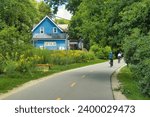 Small photo of Madison, Wisconsin, USA - Aug. 1 2023: Summer landscape of cyclists using a trail through a lush green neighborhood passing a house with "Go Solar" signage on one side in Madison, WI.