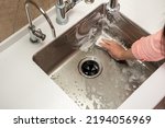 Girl washing a steel sink with a sponge and foam in the kitchen