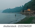 Small photo of Seattle, WA, USA - August 20, 2018: BNSF freight train traveling through Carkeek Park during a smoky evening with single man fishing in puget sound