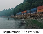 Small photo of Seattle, WA, USA - August 20, 2018: BNSF freight train traveling through Carkeek Park during a smoky evening with single man fishing in puget sound