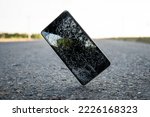 Small photo of Mobile phone falling and crashes on asphalt, broken smartphone flying down to ground. Smashed, destroyed, damaged cellphone. Accident with gadget concept. Device need repairing. Crash test