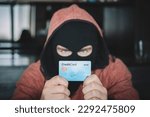 Skilled masked criminal using a stolen credit card to buy things online. A thief in a black mask holds a stolen bank card in his hands.