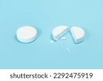Small photo of Two pills on a blue background, medicine,one tablet is broken in half. round tablet was divided equally