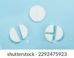 Small photo of White pills on blue background. Few pills broken in half, reducing the dose of the medicine. round tablet was divided equally