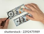 Small photo of Counterfeiter forges banknotes. Fake concept. Fake money American dollars, magnifier. view money under a magnifying glass. watermark, water mark. search for counterfeit bills