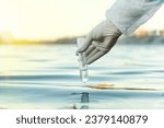 Small photo of Fence, check the water sample for infections. Gloved hand with flask and a test tube on a background of lake, river, sea. Pollution of ecology, environment
