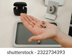 Small photo of Modern miniature hearing aids. Small and discreet invisible hearing aids in hands. Closeup of patient. Hearing rehabilitation clinic